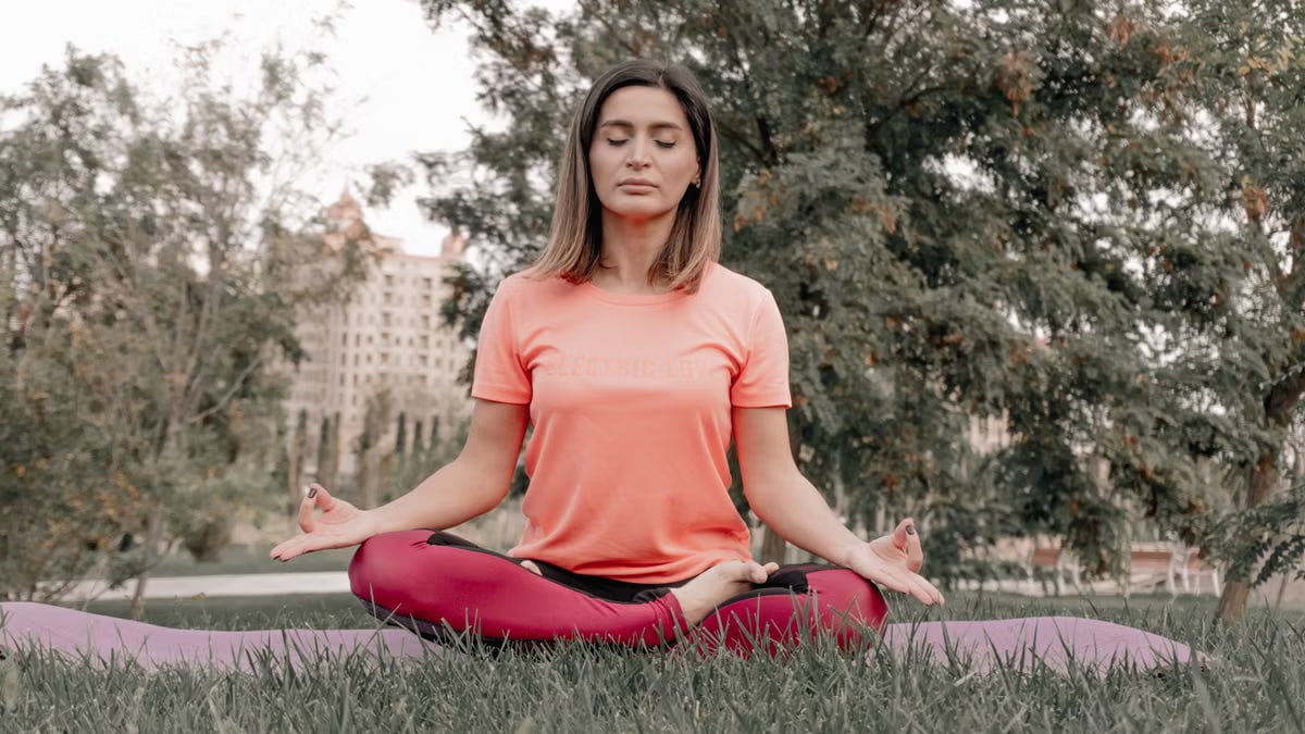 Adult woman practicing meditation on a yoga mat outdoors in a tranquil park setting.
